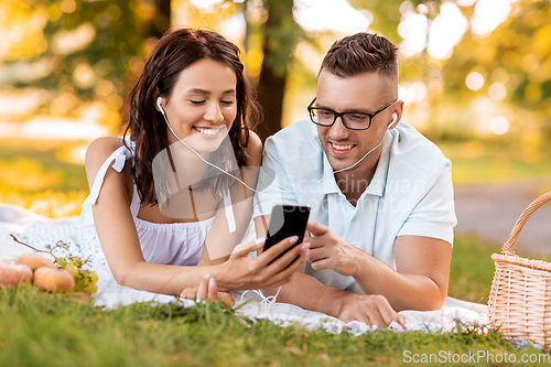 Image of couple with earphones and smartphone at picnic