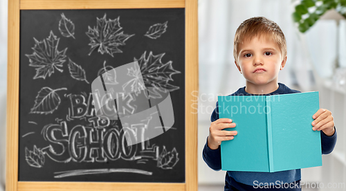 Image of little displeased student boy with book