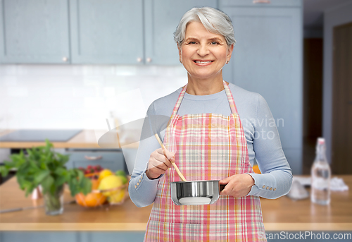 Image of senior woman in apron with pot cooking food