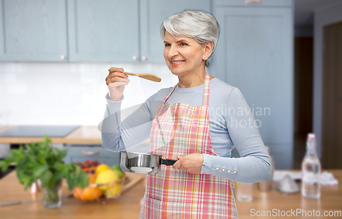 Image of senior woman in apron with pot cooking food