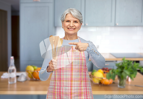 Image of smiling senior woman in apron with wooden spoons