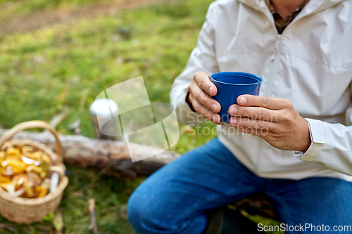 Image of man with basket of mushrooms drinks tea in forest
