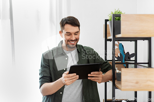 Image of happy smiling man with tablet pc at shelf at home