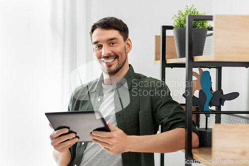 Image of happy smiling man with tablet pc at shelf at home