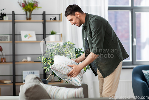 Image of happy smiling man arranging sofa cushions at home