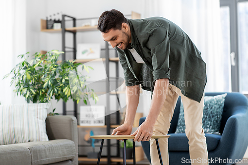 Image of man placing coffee table next to sofa at home