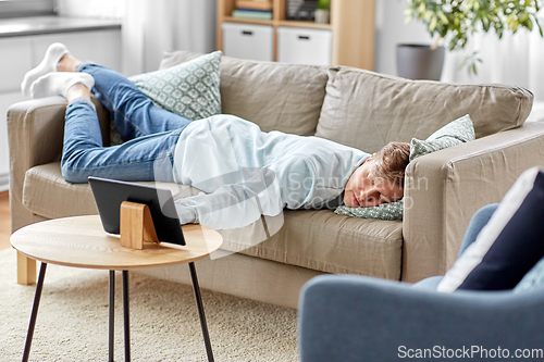 Image of bored man with tablet pc lying on sofa at home