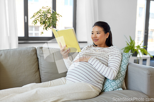 Image of happy pregnant woman reading book at home