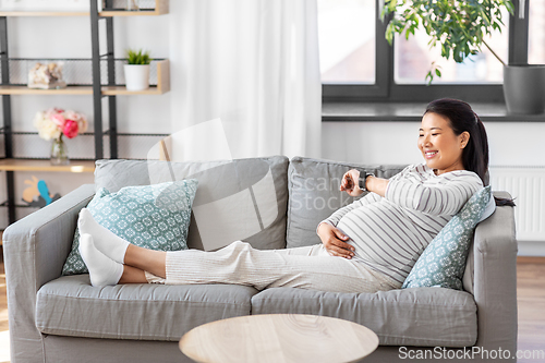 Image of happy pregnant woman with smart watch at home