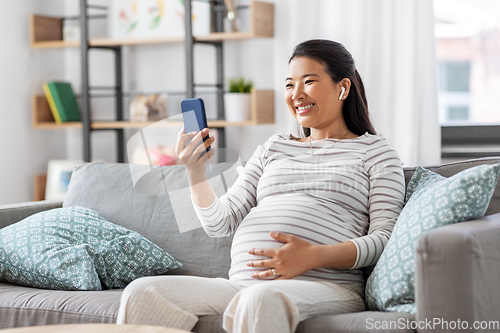 Image of pregnant woman with phone and earphones at home