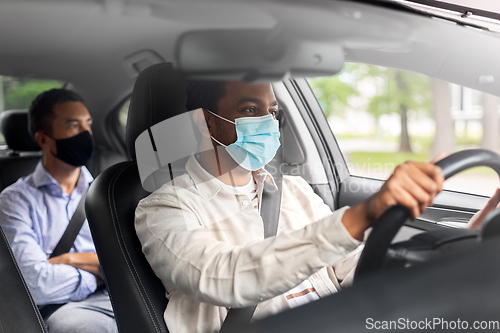 Image of male driver in mask driving car with passenger