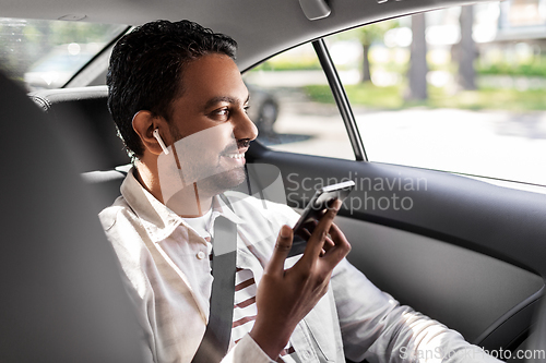 Image of passenger with earphones and cellphone in taxi car