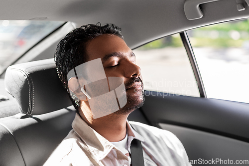 Image of indian male passenger with earphones in taxi car