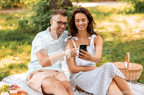 Image of happy couple with smartphone at picnic in park