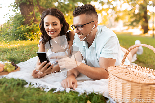 Image of couple with earphones and smartphone at picnic