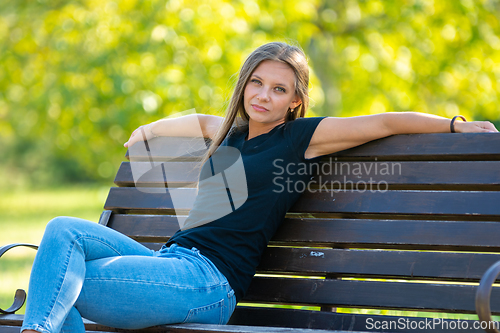 Image of A girl sits on a bench in a sunny park and looks into the frame