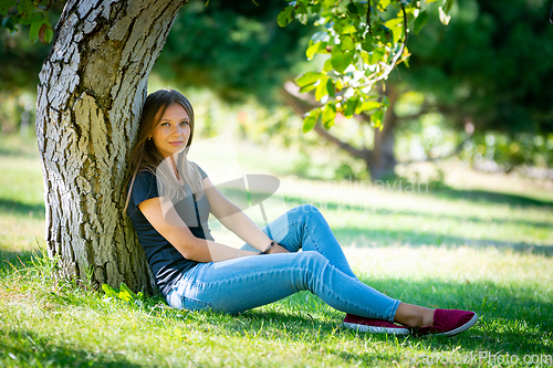 Image of A girl sits under a tree in a sunny park and looks into the frame