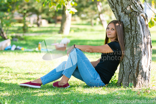 Image of A girl sits under a tree in a sunny park and joyfully looks into the frame