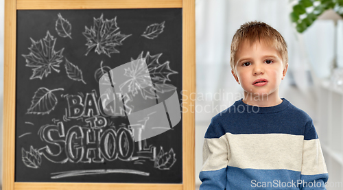 Image of bored little student boy over school blackboard