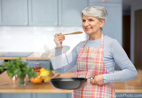 Image of smiling senior woman in apron with frying pan