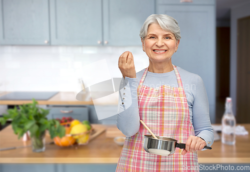 Image of senior woman in apron with pot cooking food
