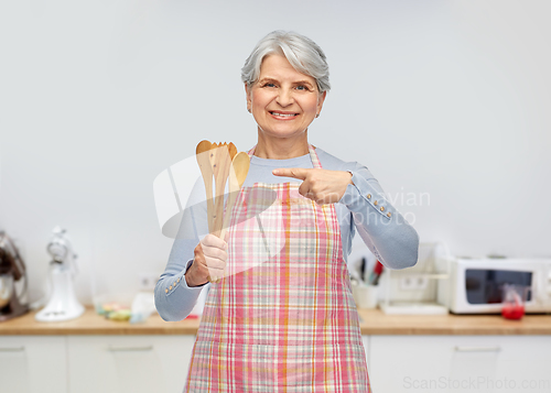 Image of smiling senior woman in apron with wooden spoons
