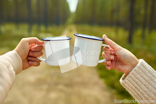 Image of couple clinking white tea mugs in forest