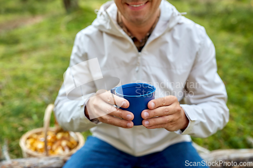 Image of man with basket of mushrooms drinks tea in forest