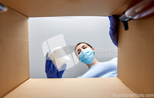 Image of woman in mask unpacking parcel box with cosmetics