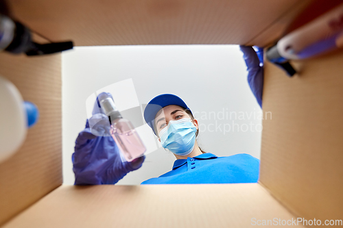 Image of woman in mask packing parcel box with cosmetics