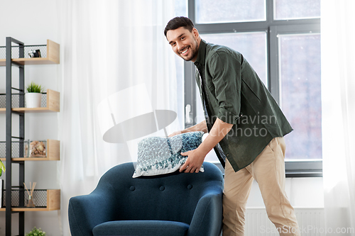 Image of happy smiling man arranging chair cushion at home