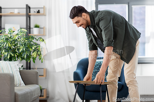 Image of man placing coffee table next to sofa at home