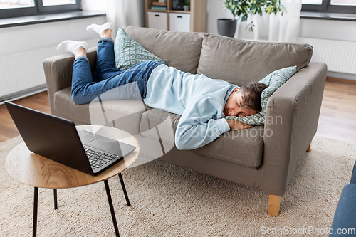 Image of bored man with laptop lying on sofa at home