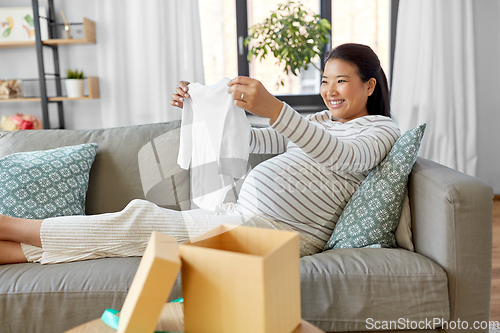 Image of happy pregnant woman with baby's bodysuit at home