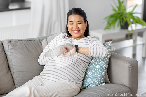 Image of happy pregnant woman with smart watch at home