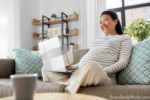 Image of happy pregnant asian woman with laptop at home