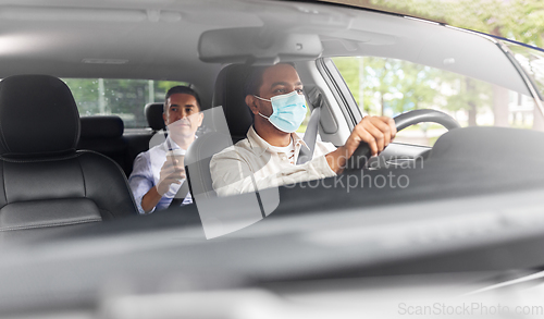 Image of male driver in mask driving car with passenger