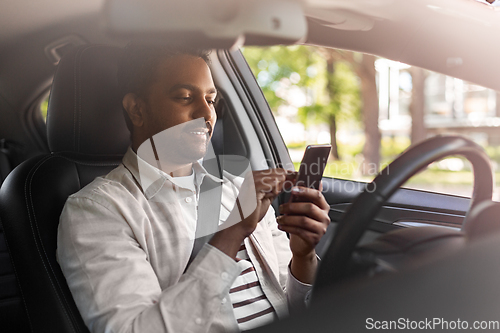 Image of smiling indian man in car using smartphone