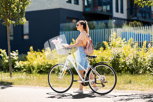 Image of woman with flowers in bicycle basket in city