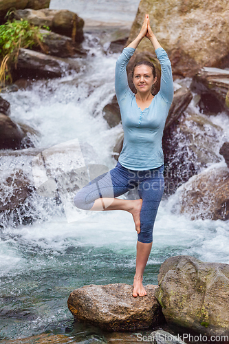 Image of Woman in yoga asana Vrikshasana tree pose at waterfall outdoors