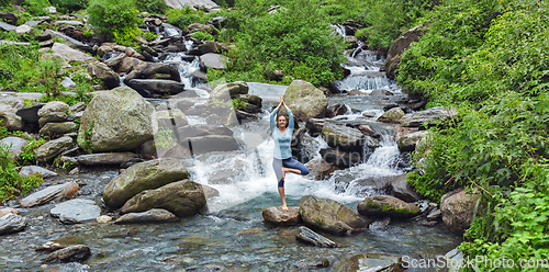 Image of Woman dpoing yoga asana tree pose at waterfall