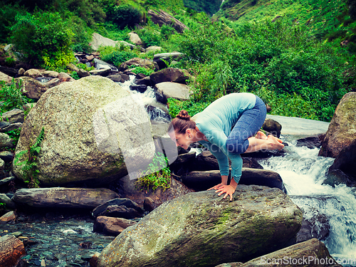 Image of Woman doing Kakasana asana arm balance at waterfall