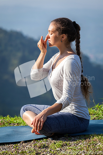 Image of Woman practices pranayama in lotus pose outdoors