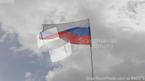 Image of Russian flag on the flagpole waving in the wind against a blue sky with clouds. Slow motion