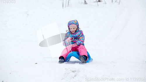 Image of Cheerful girl riding a sled downhill on a snow covered sledge trail in a white sunny winter mountain landscape