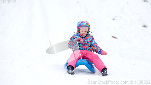 Image of Cheerful girl riding a sled downhill on a snow covered sledge trail in a white sunny winter mountain landscape