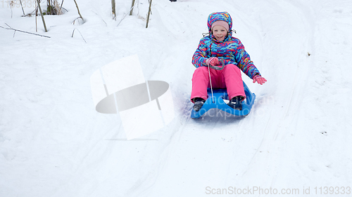 Image of Cheerful girl riding a sled downhill on a snow covered sledge trail in a white sunny winter mountain landscape