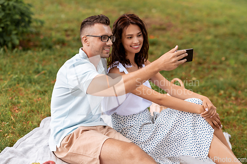 Image of happy couple taking selfie at picnic in park
