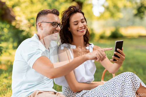 Image of happy couple with smartphone at picnic in park