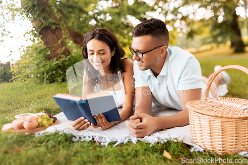 Image of happy couple reading book on picnic at summer park